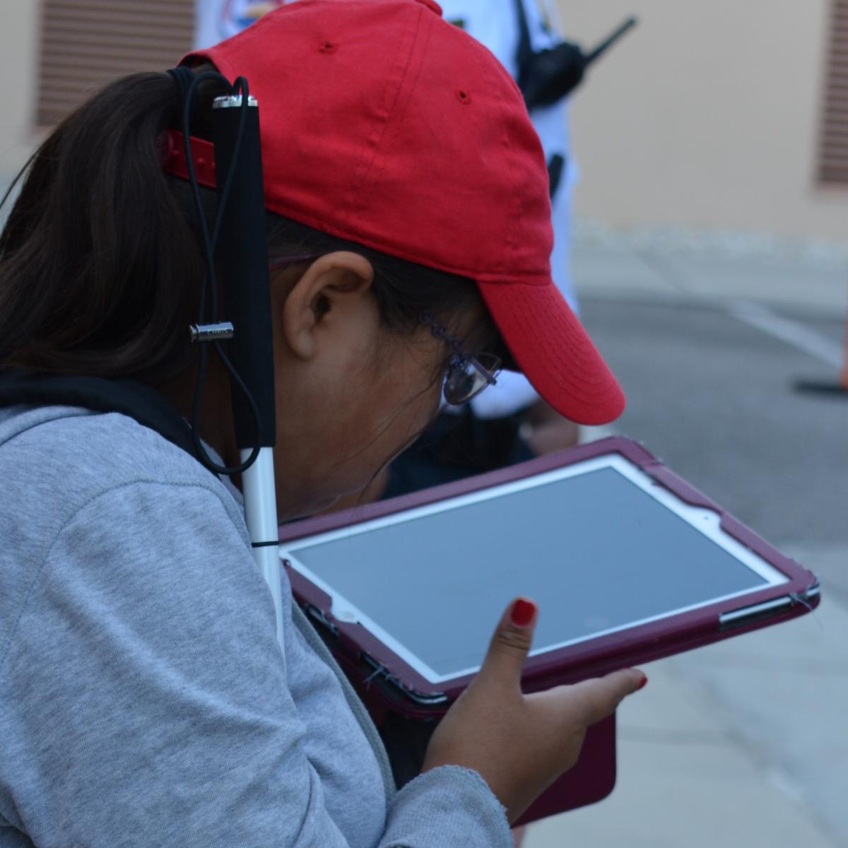 a girl holding her cane looking at an iPad