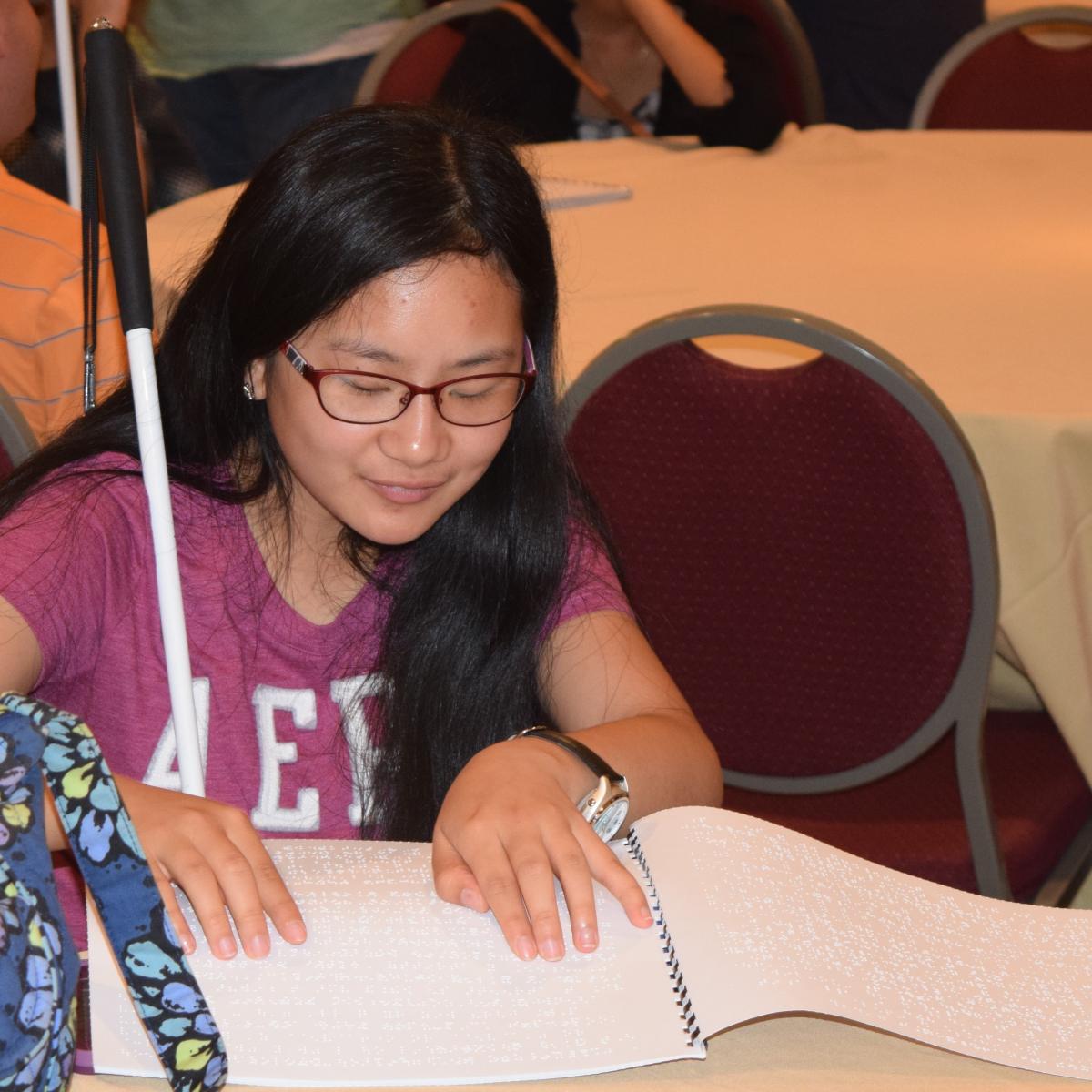 a teen girl reading braille at a table